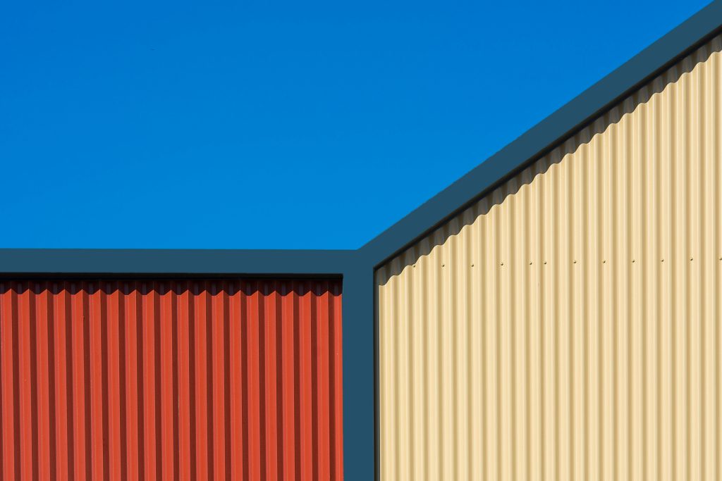 A modern building facade with red and beige corrugated iron against a clear blue sky.